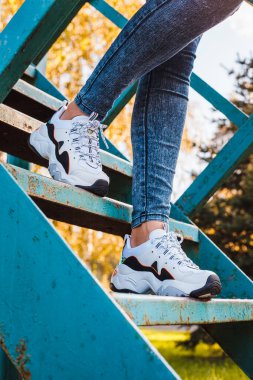 Parktaki demir merdivenlerde kot pantolon giymiş siyah bacaklı beyaz spor ayakkabılar.