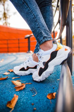 Kotlu, beyaz spor ayakkabılı, siyah pantolonlu demir çitin yanında duran bir kızın bacakları.