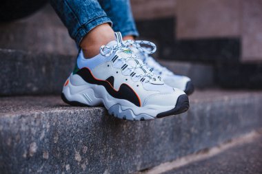 Sokakta mermer bir merdivende kot pantolon giymiş siyah bacaklı beyaz spor ayakkabılar.