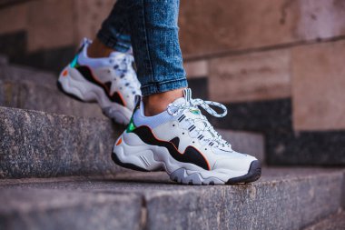 Sokakta mermer bir merdivende kot pantolon giymiş siyah bacaklı beyaz spor ayakkabılar.