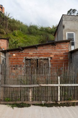 Dikey bambu çubuklardan yapılmış, kırmızı tuğlalı duvarın önünde duran ve el yapımı inşaat malzemelerini gösteren kırsal bir çit..