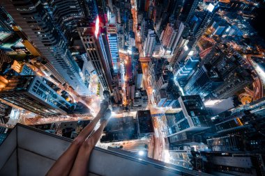Hong Kong'da bir gökdelenin çatı kenarında oturan kız