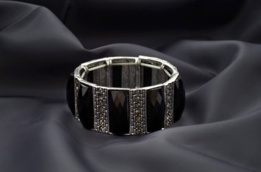 Saten koyu arka plan üzerinde siyah taşlar ile gümüş bilezik