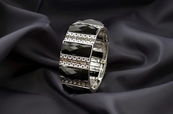 Pulsera de plata con gemas negras sobre fondo satinado oscuro — Foto de Stock