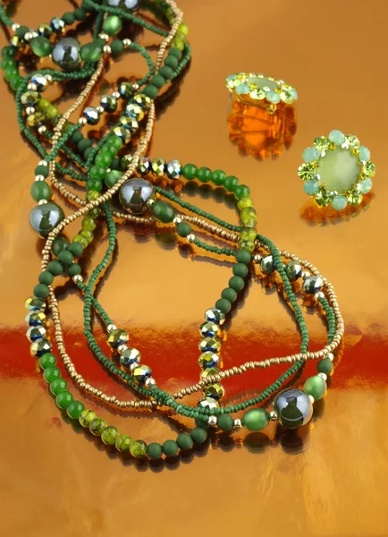 Joyería de moda con diamantes de imitación verdes sobre fondo naranja espejo — Foto de Stock