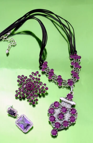 Jóias de moda de prata com strass roxo no fundo espelhado verde — Fotografia de Stock