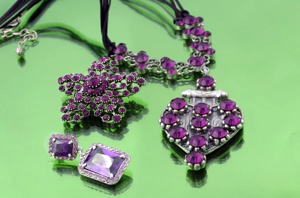 Jóias de moda de prata com strass roxo no fundo espelhado verde — Fotografia de Stock