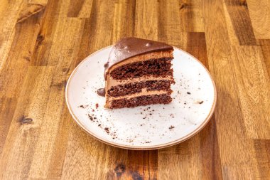 Portion of three chocolates cake seen from the front on a white plate and on a table of oak boards