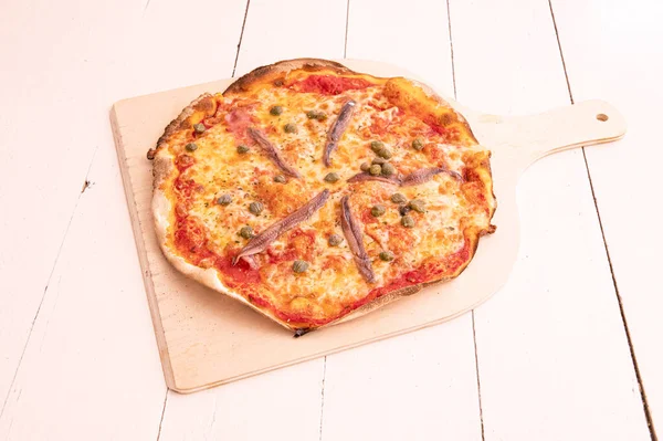 Pizza with anchovies on wooden board placed on white wooden table