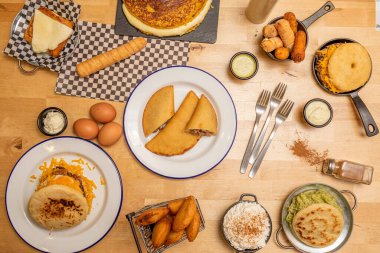 Açık ahşap masada tipik Venezuela yemekleri. Arepas, cachapas, tequeos, corn empanadas, egg and sos