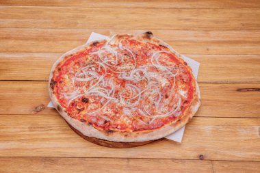 Pastırma ve soğanlı pizza. Yağ geçirmez kağıt üzerinde. Hafif ahşap masanın üstünde.