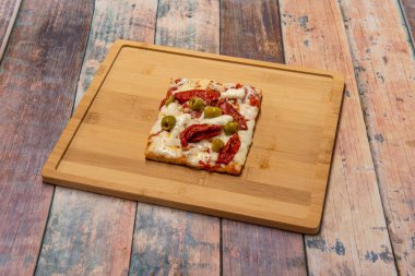 Kurutulmuş domates, zeytin, mozarella peyniri, hamur ve domatesli kare pizza.