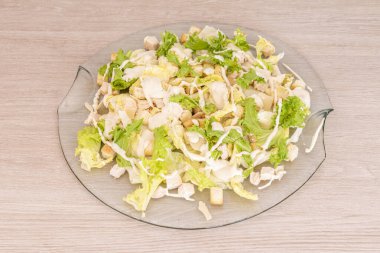 Generous portion of Caesar salad with croutons, chicken and lettuce in a transparent glass plate