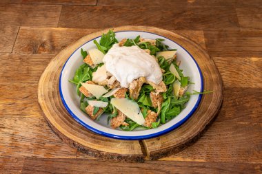 Caesar salad with fresh ingredients, croutons, arugula and Manchego cheese slices on wooden slice trivet