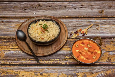 Basmati pilavlı siyah kase ve tavuk tikka masala, siyah kaşık ve tahta kaşık.