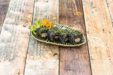 Deniz kabuğu, avokado ve yeşil tabakta doğranmış soğan ile doldurulmuş siyah pirinç rulosu.