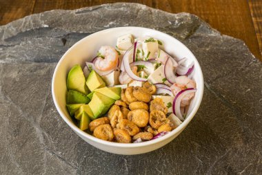 Büyük kızarmış mısır taneleri ve avokado küpleriyle beyaz bir kase balık ve karides ceviche.