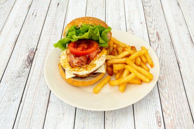 Yumurtalı, peynirli, marullu, pastırmalı ve yanında patates kızartması olan harika bir hamburger.