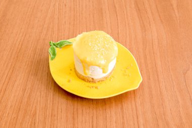 Limon şeklindeki ve ahşap masadaki renkli tabakta limon kremalı cheesecake.