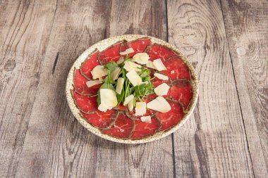 Tipik İtalyan etli carpaccio roka ve gri masada parmesan peynirli gevrek.