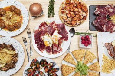 Great Spanish Tapas top view with radishes and cutlery on light wooden table