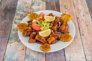 Colombian picapollo with male plantain tostones and a little salad with tomato and red onion and some lemon wedges