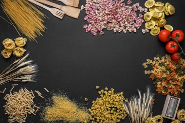 makarnanın, domateslerin ve mutfak gereçlerinin siyah arka planda olduğu kompozisyon