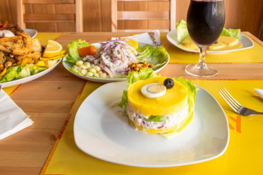 Peru restoranının tabakları ceviche, jalea ve Lima Cause gibi tipik yemeklerle dolu ve sarı masa örtüleri üzerinde bir bardak chicha morada.