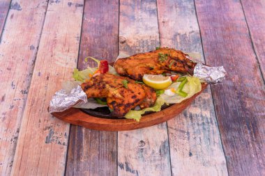 Tavuk butları, ahşap masada, alüminyum folyoyla kaynamış tabağın tepesinde, tandır usulü pişirilmiş.