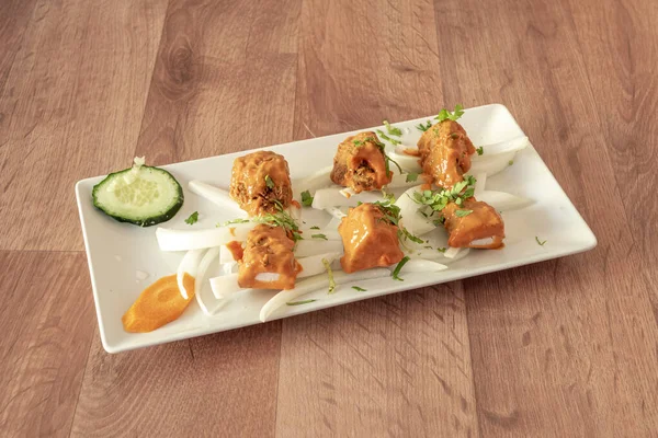 Indian chicken tikka masala recipe on pieces of white onion, cucumber, carrot, chopped parsley on a white tray