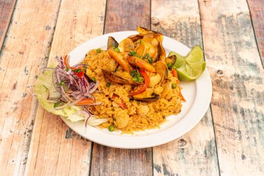 Lezzetli Peru deniz ürünleri pilavı. Karides, midye, midye, istiridye, mürekkep balığı, kırmızı soğan ve beyaz tabakta limon.