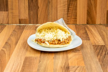 Arepa pelua with shredded meat and a lot of grated cheese on wooden background clipart