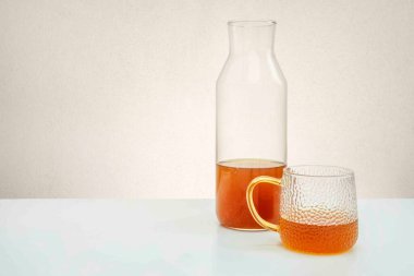 Açık mavi masa ve beyaz zemin üzerinde limon çayı bulunan şişe ve şeffaf cam.