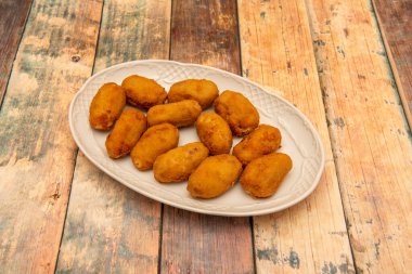 Beyaz porselen tepside bol miktarda serrano jambonu ve ahşap bir masada morina balığı var.