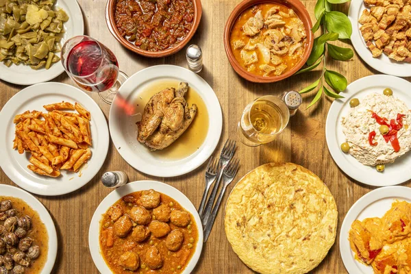 Top view image of spanish dishes and tapas, tortilla, salad, roast chicken, bordeaux meatloaf, green beans, torreznos, snails and wooden table
