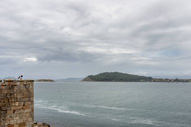 Duvarın tepesinden bulutlu bir günde okyanus ufkunu izleyen insanlar.