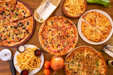 Tahta masanın üzerinde soğan, domates ve patates kızartması ile dilimlenmiş bir sürü pizza.