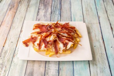 Serrano jambonu ve beyaz tabakta patates kızartmasıyla kırılmış yumurtalardan oluşan tipik ve süper ünlü İspanyol tapaları.