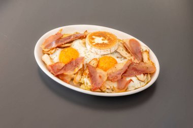 Kızarmış pastırmalı yumurta tepsisi, keçi peyniri ve gri masada maydanoz.