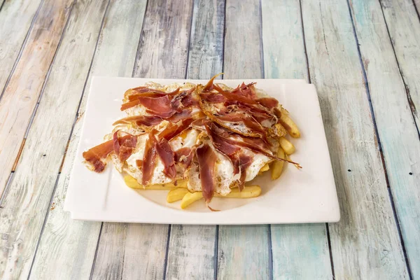 Serrano jambonu ve beyaz tabakta patates kızartmasıyla kırılmış yumurtalardan oluşan tipik ve süper ünlü İspanyol tapaları.