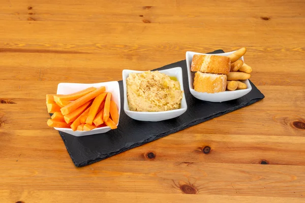 Nohut humusu, zeytin yağı ve susamlı bir başlangıç yanında da ahşap bir masaya daldırmak için havuç şeritleri, kızarmış ekmek ve ekmek.