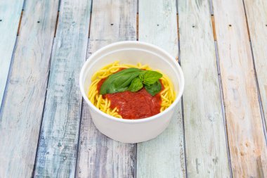 Pomodoro soslu spagetti tarifi ve ahşap masada fesleğen.