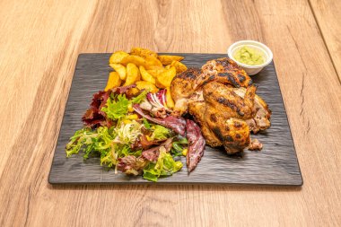 Kömür kızartılmış tavuk, lahana salatası, lüks patates kızartması ve siyah tabakta biraz guacamole.