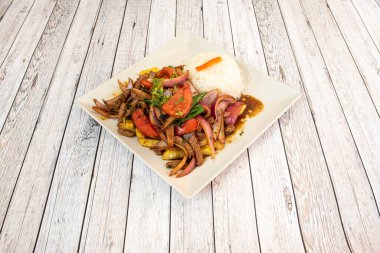 Delicious lomo  recipe with sauted pork tenderloin, white rice, onion and pepper and homemade chips with roast beef juice on white square plate