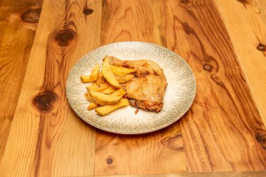 Kızarmış tavuk budu ve ahşap masada süslü patates.