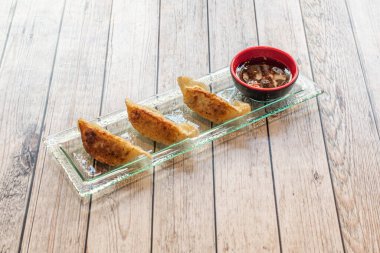 Kızarmış gyozas aperatifi. Soya soslu. Hafif ahşap masadaki cam tepside.