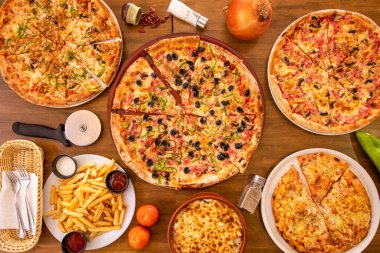 Tipik İtalyan yemeklerini, dilimlenmiş pizzaları, patatesleri, soğanları, çatal bıçakları ve domatesleri ahşap masa üzerinde tuz ve biberle en üst düzeyde görmek