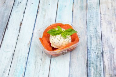 Taze burrata peyniri, domates, biber ve fesleğen dilimleri, ahşap arka plandaki eve servis paketinde.