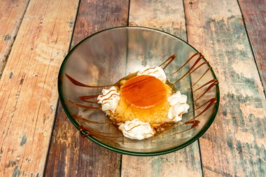 Ahşap zemin üzerinde cam bir kasenin içinde kremalı ve karamel kaplı nefis ev yapımı yumurta kreması.