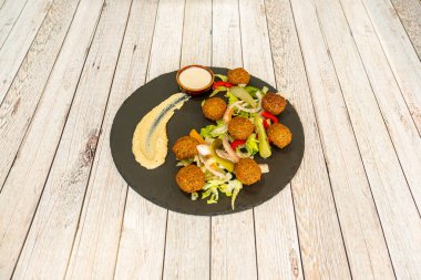 Marul salatalı falafel topları ve siyah bir tabakta nohut ve turşu turşusu.